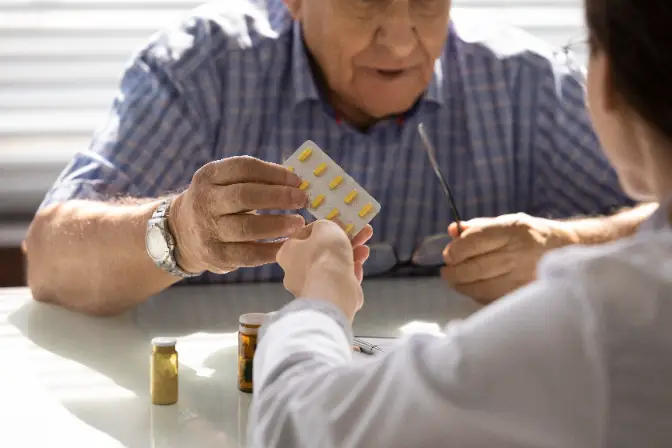 Bild einer Betreuungskraft, der einem älteren Menschen Medikamente gibt und ihm dabei hilft, die ärztlichen Anweisungen zu befolgen.